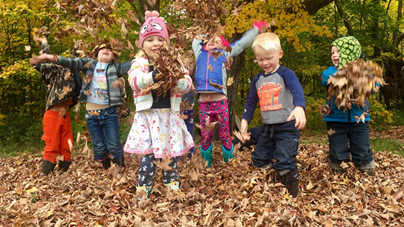 Barn som leker med l&ouml;v p&aring; en f&ouml;rskola.