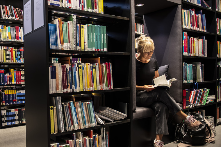 Kvinnlig student sitter och läser en bok i biblioteket.