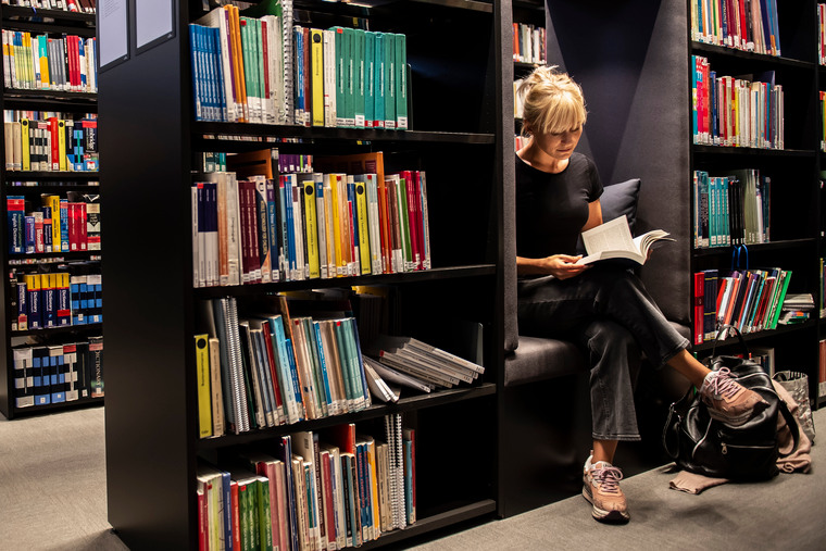 Kvinnlig student sitter och läser en bok i biblioteket.