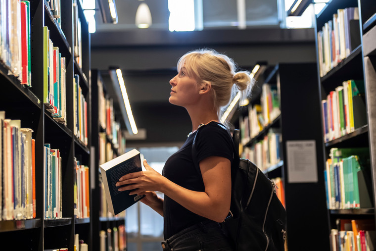 Kvinnlig student letar efter en bok bland bokhyllorna i biblioteket.
