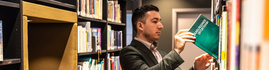 Manlig student letar efter en bok bland bokhyllorna i biblioteket.