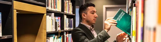 Manlig student letar efter en bok bland bokhyllorna i biblioteket.