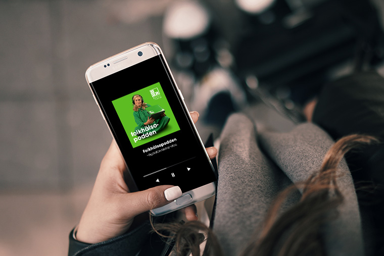 En hand som håller i en mobil där folkhälsopodden spelas