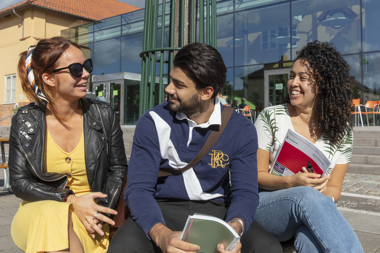 Tre studenter sitter utomhus på en bänk.