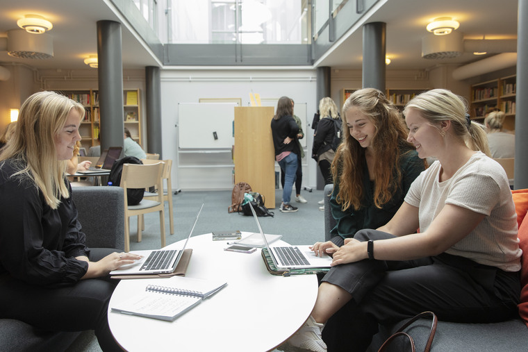 Tre tjejer sitter i grå soffa i biblioteket.