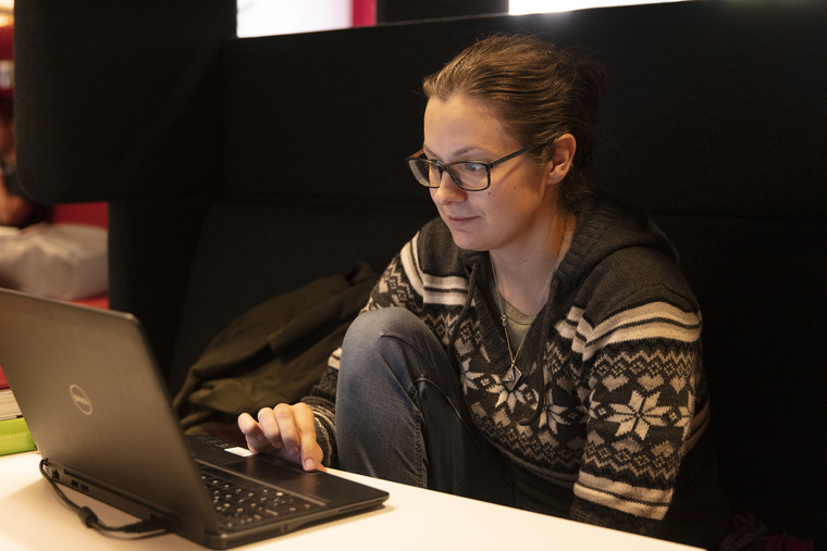 Tjej sitter med dator i grå soffa.