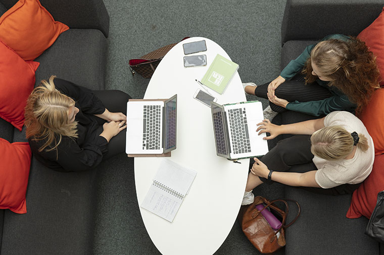 Tre studenter vid vitt bord studerar tillsammans.