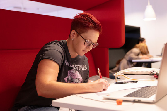 Tjej sitter i röd soffa och skriver med dator framför sig.