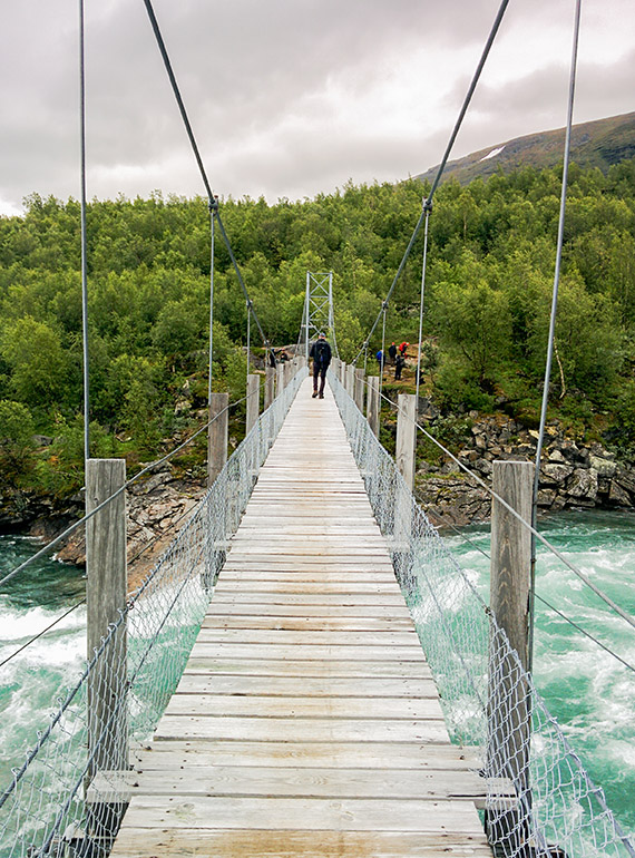 Tv&aring; personer &aring;t g&aring;ngen f&aring;r passera &ouml;ver den 61 meter l&aring;nga h&auml;ngbron &ouml;ver &auml;lven Vuojat&auml;dno. Dagsturen g&aring;r mot Hambergs glaci&auml;r. Foto: Johanna Gr&ouml;nroos