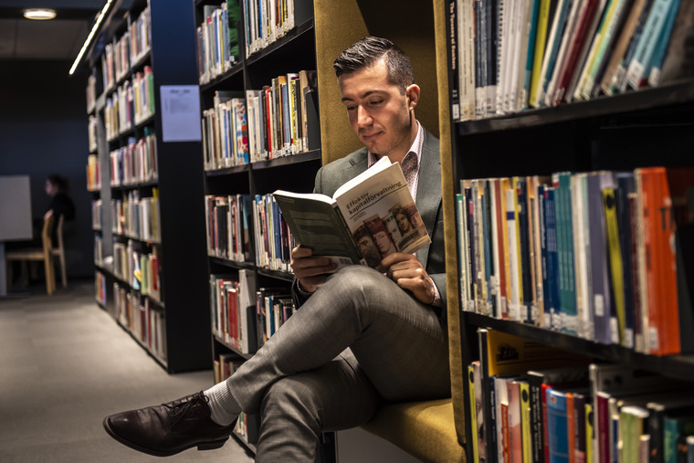 Manlig student sitter och läser en bok i biblioteket.