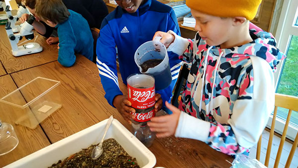 Med hj&auml;lp av en delad l&auml;skflaska, sand och gr&ouml;vre grus bygger barnen minireningsverk f&ouml;r att se hur man kan filtrera bort saker fr&aring;n vattnet.