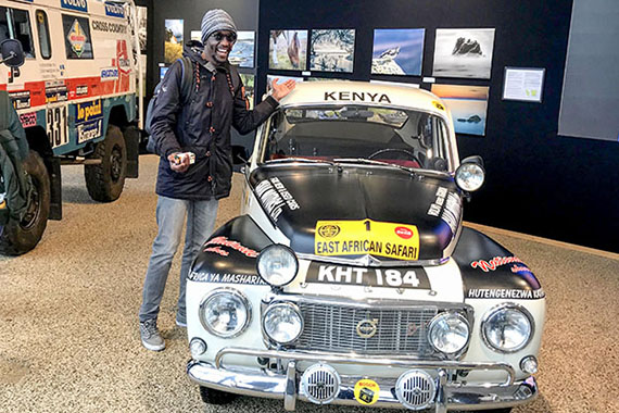 Pascal standing beside a vintage car with a sign that says Kenya on it