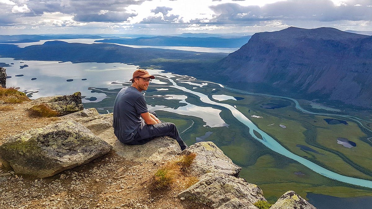 Artikelf&ouml;rfattaren sitter p&aring; Skierffes kant och k&auml;nner vindarna nere fr&aring;n Rapadalen pressa mot f&ouml;tterna. Efter tv&aring; dagars vandring infinner sig en k&auml;nsla av att vara vid v&auml;rldens &auml;nde och mittpunkt p&aring; en och samma g&aring;ng. Foto: Johanna Gr&ouml;nroos