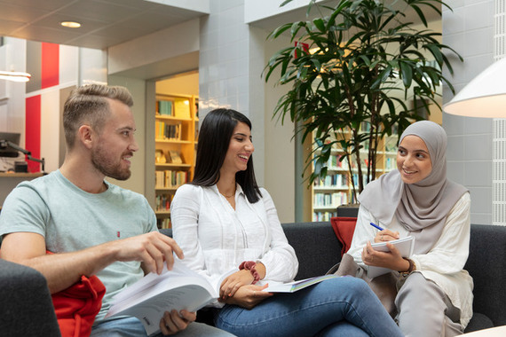 En kille och två tjejer sitter i soffan i biblioteket.