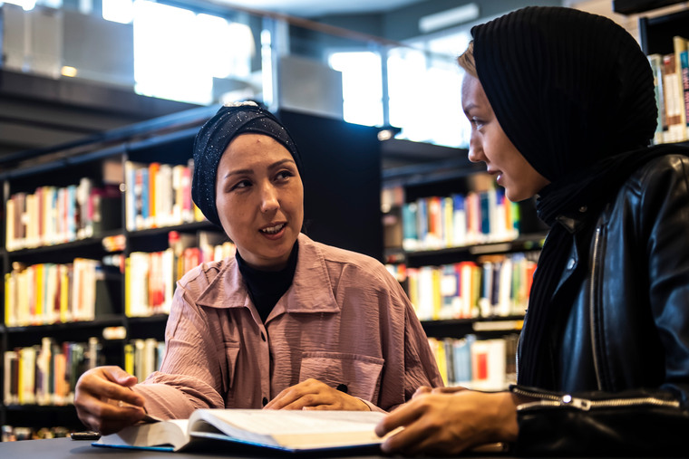 Två kvinnliga studenter sitter vid ett bord i biblioteket.
