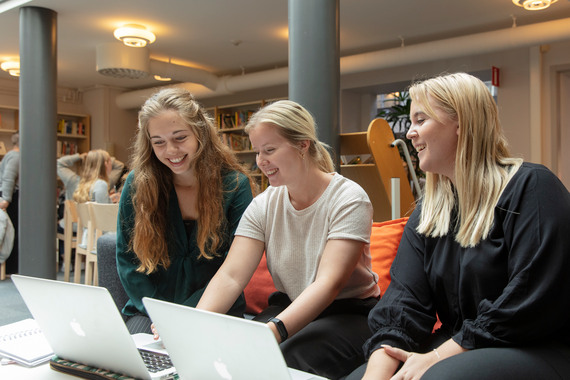Tre tjejer sitter i grå soffa i biblioteket.