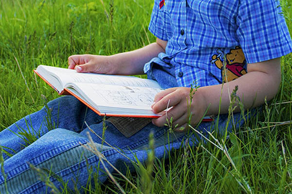 Pojke läser bok i gräset.