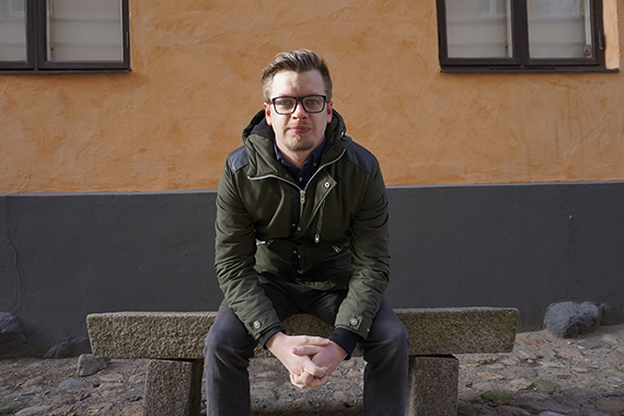 André sitter på en bänk och tittar in i kameran