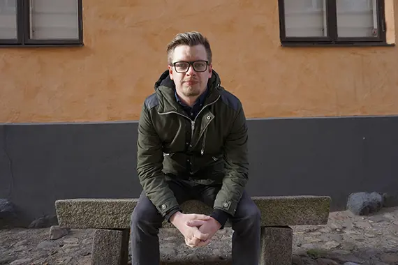 André sitter på en bänk och tittar in i kameran