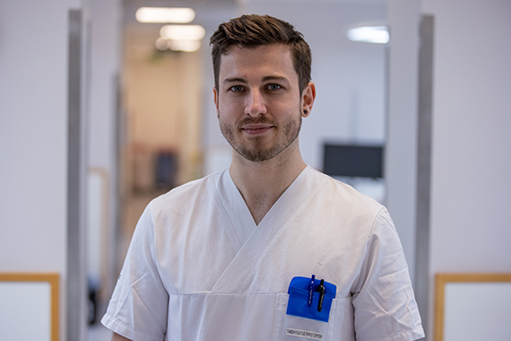 Kristoffer står i en korridor på tandhygienistklinik och tittar in i kameran