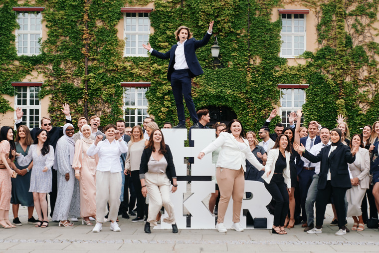 Glada studenter vid stora vita bokstäver HKR på Högskolan Kristianstads campus.