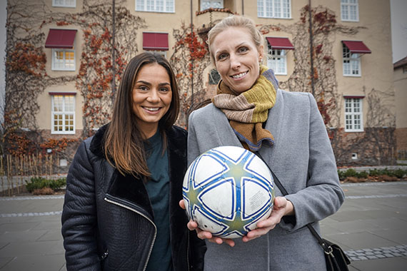 Lisa och Sandra, med en fotboll i handen, utanför ett hus på högskolan