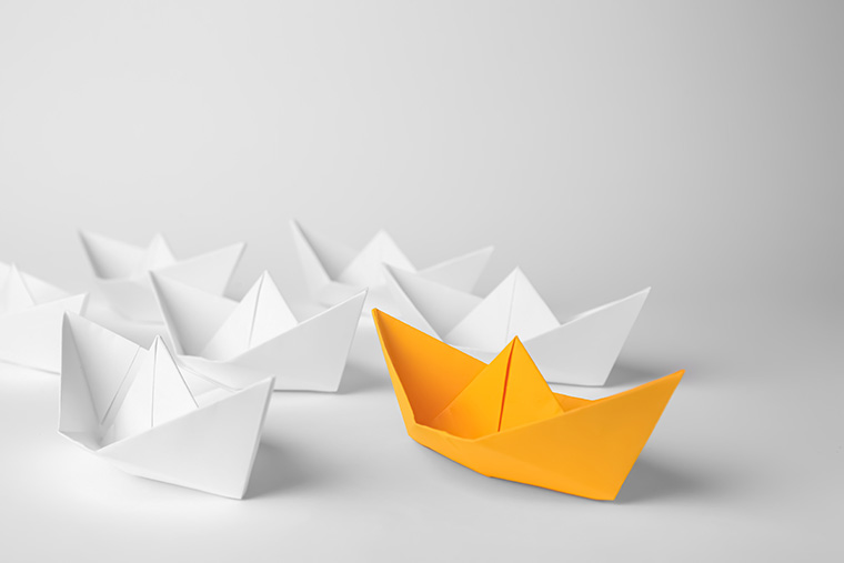 Illustration av båtar vikta av papper, en orange och resten vita.