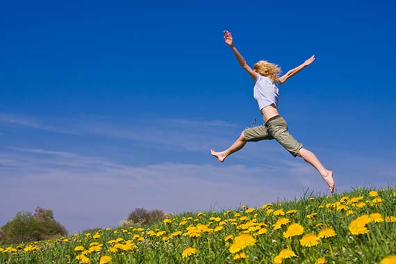 Kvinna hoppar på fält med maskrosor