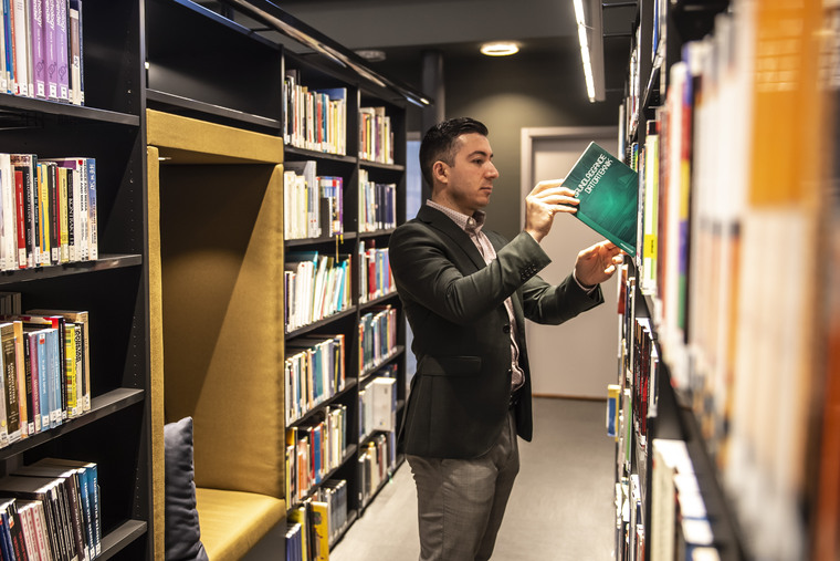 Manlig student letar efter en bok bland bokhyllorna i biblioteket.