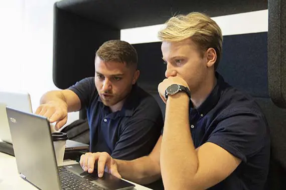 Två studenter sitter i en soffgrupp och tittar på en datorskärm