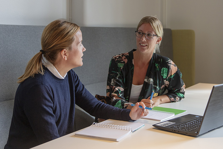 Två studenter i samtal, med anteckningsblock och laptop framför sig.