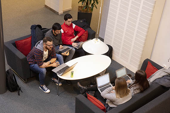 Fem studenter studerar, sitter i soffor