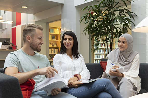 Tre glada studenter i soffa, med papper och penna