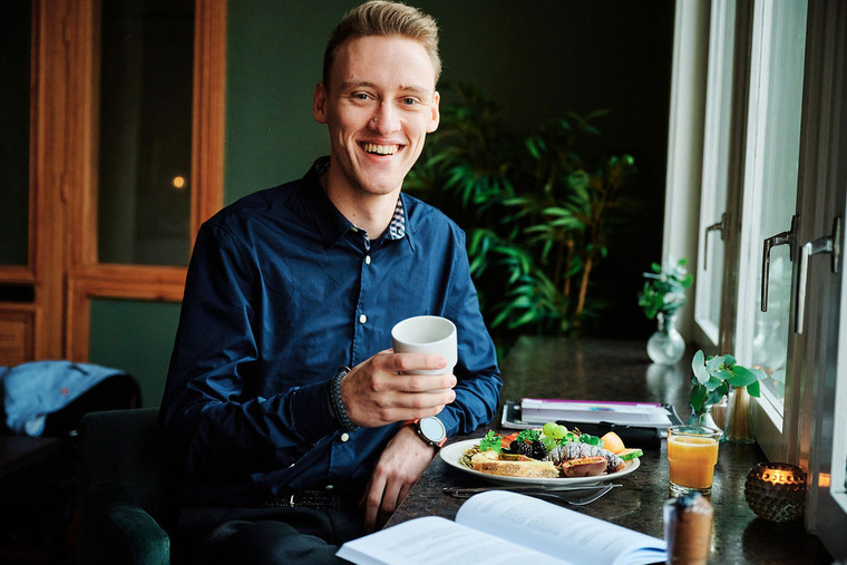 Student med kaffekopp, fat med frukt och en uppslagen bok.